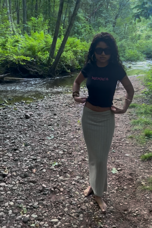 young teen adult woman wearing a babytee that reads 'menace' in pink lettering. nature background and boho theme.
