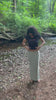 young teen adult woman wearing a babytee that reads 'menace' in pink lettering. nature background and boho theme. belly ring and white toes. crop top teen style.